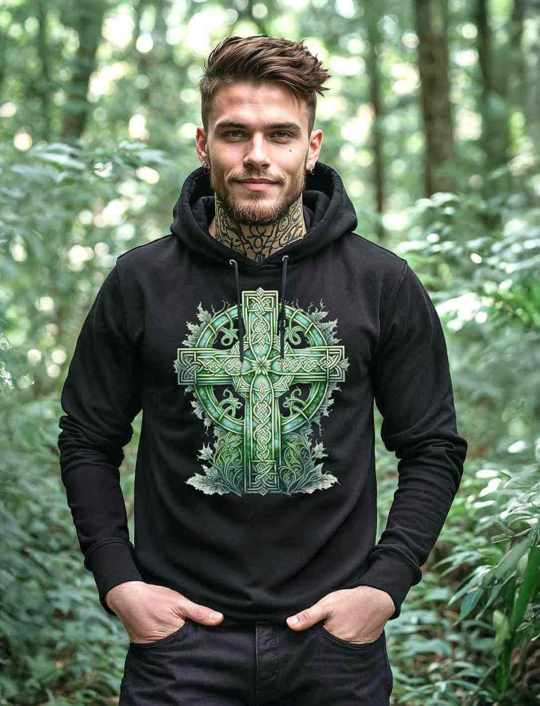 Junger Mann trägt den Celtic Cross Watercolour Hoodie in schwarz vor einem mystischen Waldhintergrund.