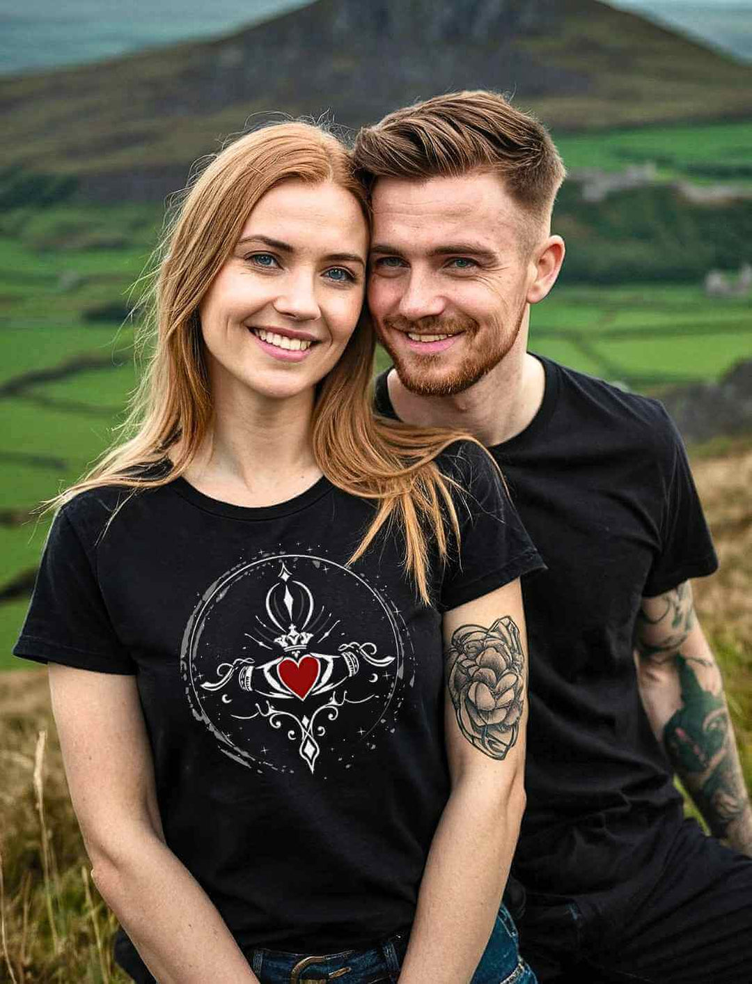 Lächelndes Paar in Hügel-Landschaft, die Frau trägt ein T-Shirt mit dem Design „Claddagh – Symbol der ewigen Liebe“ in Schwarz