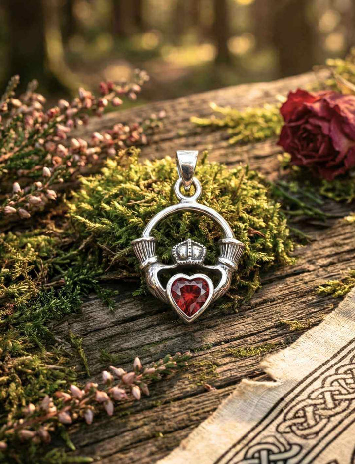 Claddagh Medaillon aus 925 Silber mit rotem Herzstein, arrangiert auf Moos und Holz