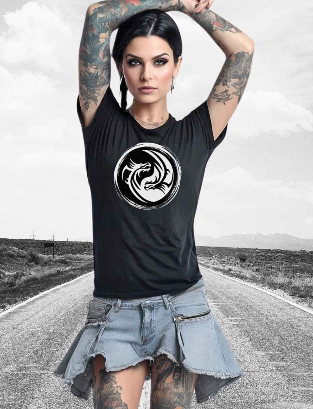 Frau mit Tattoos trägt ein schwarzes 'Drachensiegel des Gleichgewichts' T-Shirt mit Yin-Yang-Drachenmotiv, posiert vor einer unscharfen Straßenlandschaft