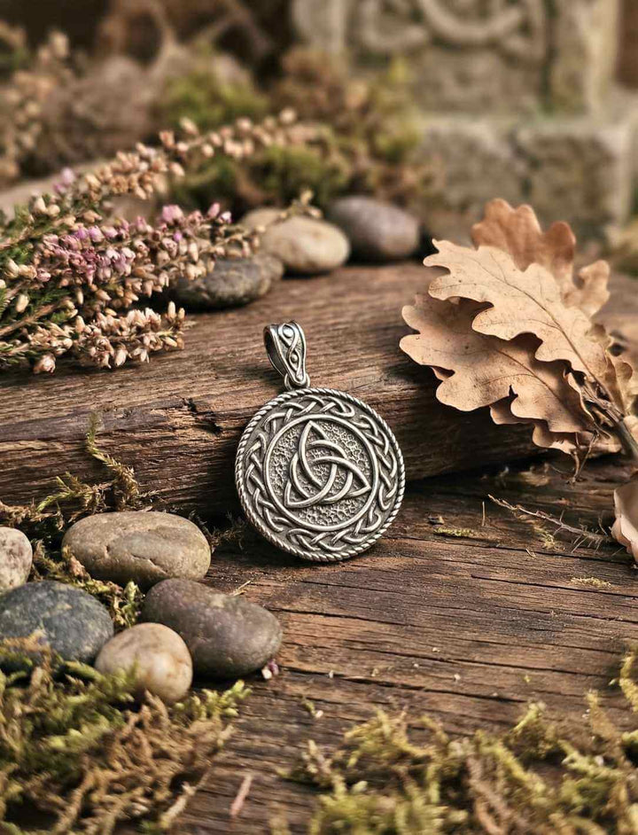 Keltischer Triquetra Anhänger mit Flechtrahmen, liegend auf Holz mit Steinen, Moos und Herbstblättern