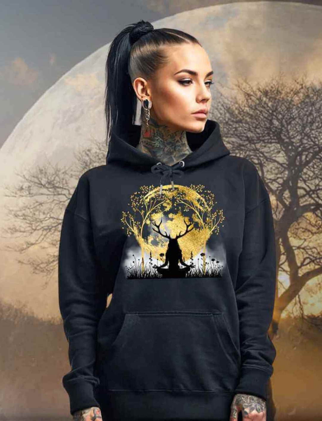 Junge Frau im 'Druidin der alten Wälder' Organic Unisex Hoodie in Schwarz, vor einem mystischen Mond und einem Lebensbaum, der die tiefe Verbindung zwischen Mensch und Natur symbolisiert.