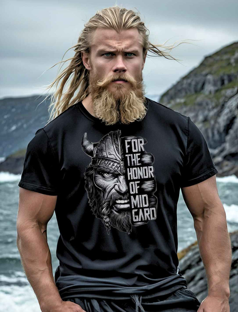 Blondhaariger Mann mit Bart trägt das schwarze 'For the Honor of Midgard' T-Shirt vor einer rauen Küstenlandschaft, sein Blick so unerschütterlich und kühn wie der eines Wikingers.