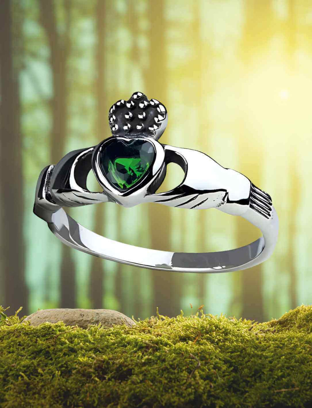 Der Claddagh-Ring mit grünem Stein, präsentiert auf einem moosbedeckten Hintergrund inmitten eines mystischen Waldes.