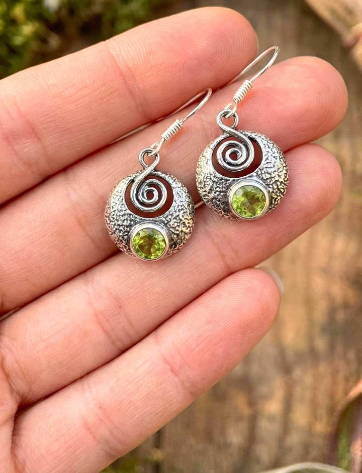 Hand hält keltische Silberohrringe mit Peridot Größenvergleich