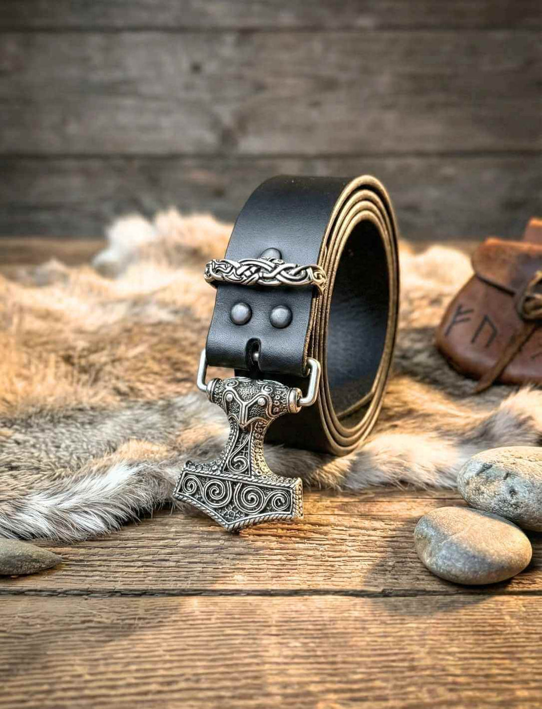 Ledergürtel Hammer des Nordens mit verzierter Thorshammer-Schnalle, aufgerollt im rustikalen Setting
