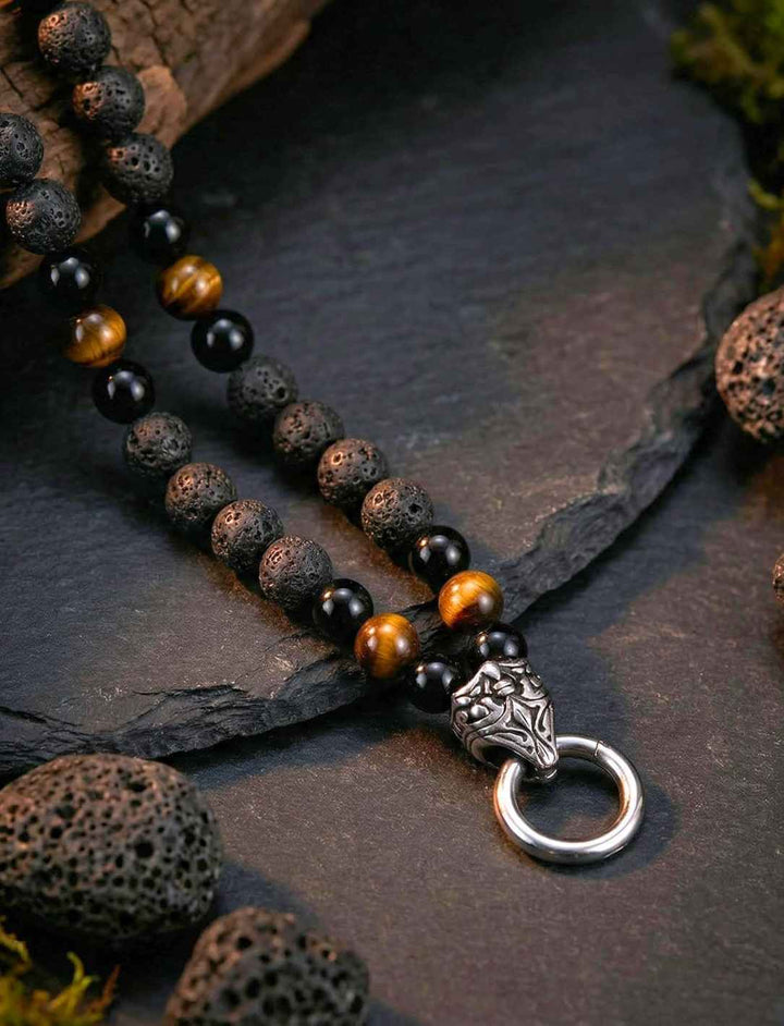 Detailaufnahme der Lavastein-Obsidian-Tigerauge-Kette mit Edelstahl-Clipring auf rauem Lavagestein