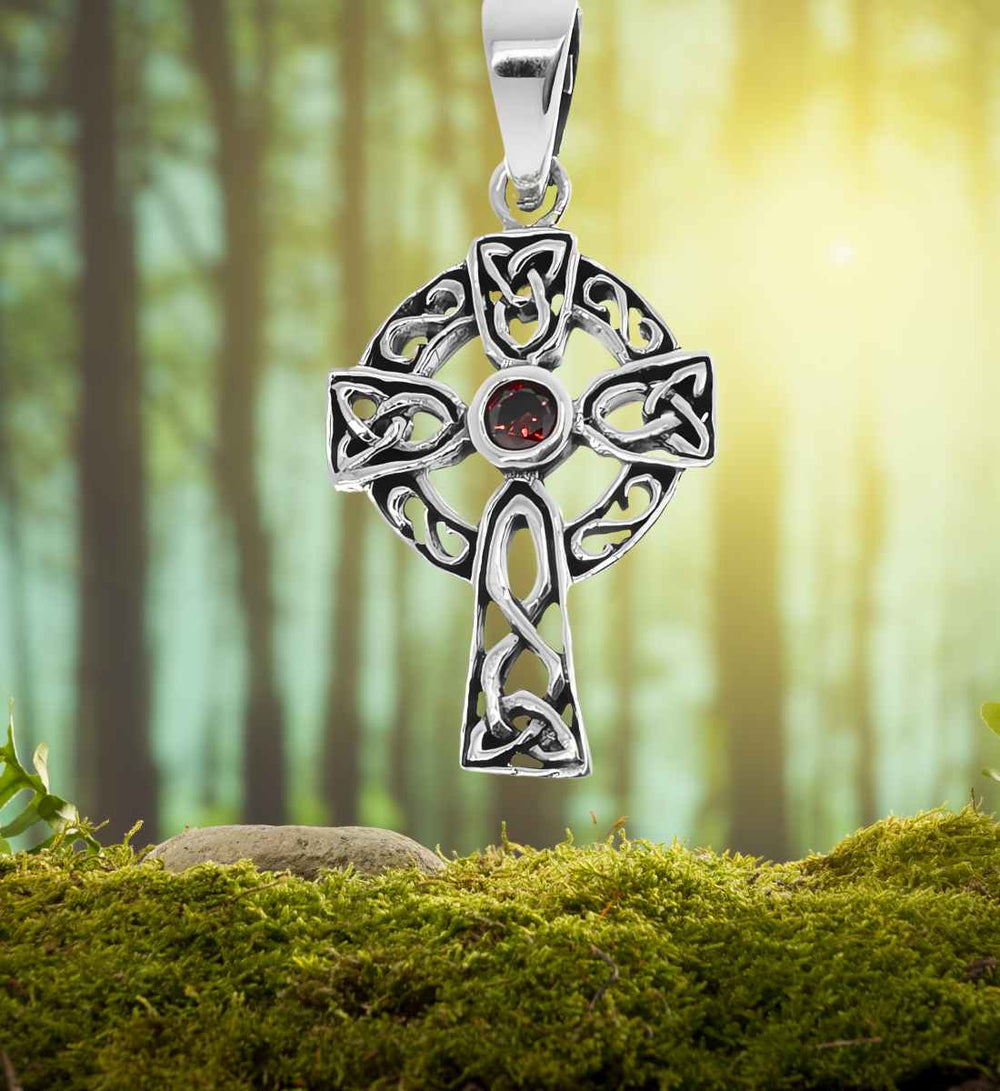 Kreuz der Roten Sonnenwende Anhänger auf einem Moos-/Waldhintergrund – Die keltischen Knoten und der leuchtend rote Stein des Anhängers stehen im Einklang mit der Natur und erinnern an die Zeitenwende im Jahreskreis.