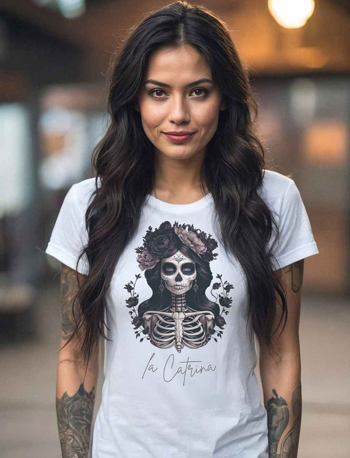 Junge Frau mit dunklem Haar trägt das “Catrina Deluxe” Damen T-Shirt in Weiß – Mystisches Design inspiriert vom Día de los Muertos, fotografiert in einer urbanen Umgebung.