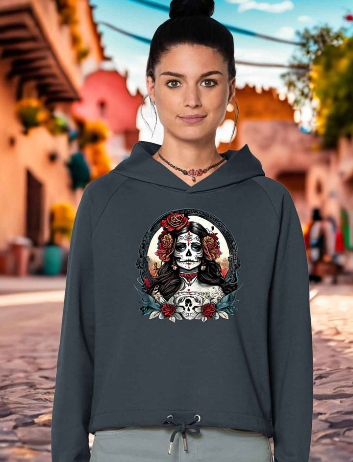 Junge Frau trägt das India Ink Grey La Catrina Cropped Hoodie, stehend auf einer charakteristischen mexikanischen Straße während des Dia de los Muertos – Runental.de.