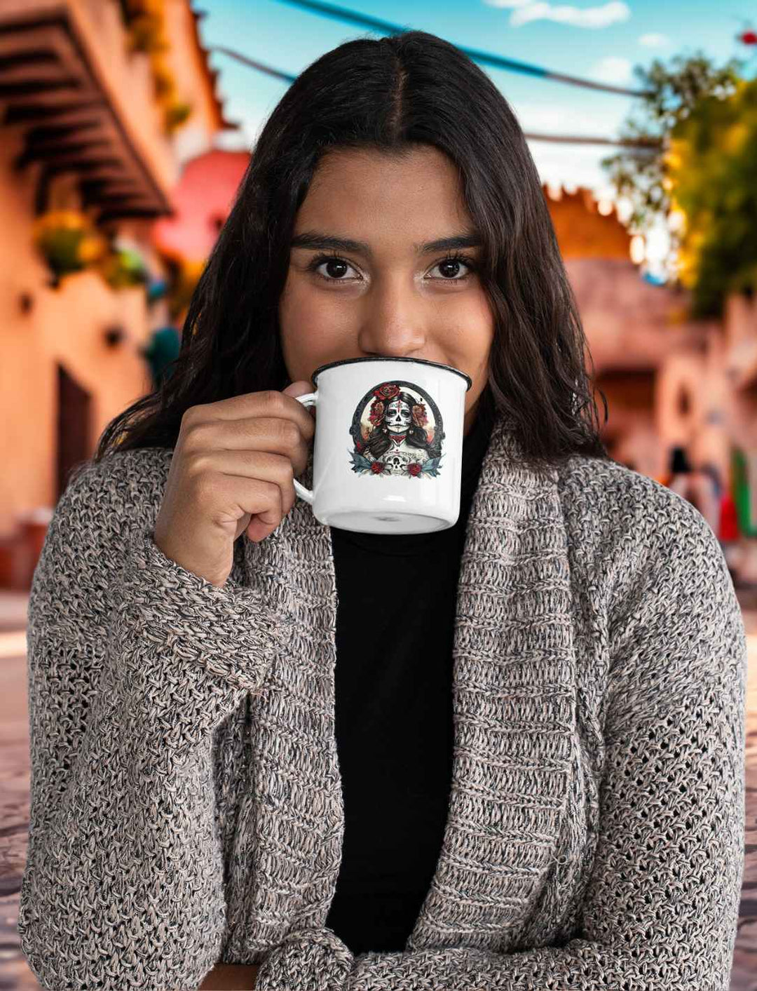 Junge Frau genießt einen Schluck aus der weißen La Catrina Emaille-Tasse, stehend auf einer typischen mexikanischen Straße während des Dia de los Muertos – Runental.de