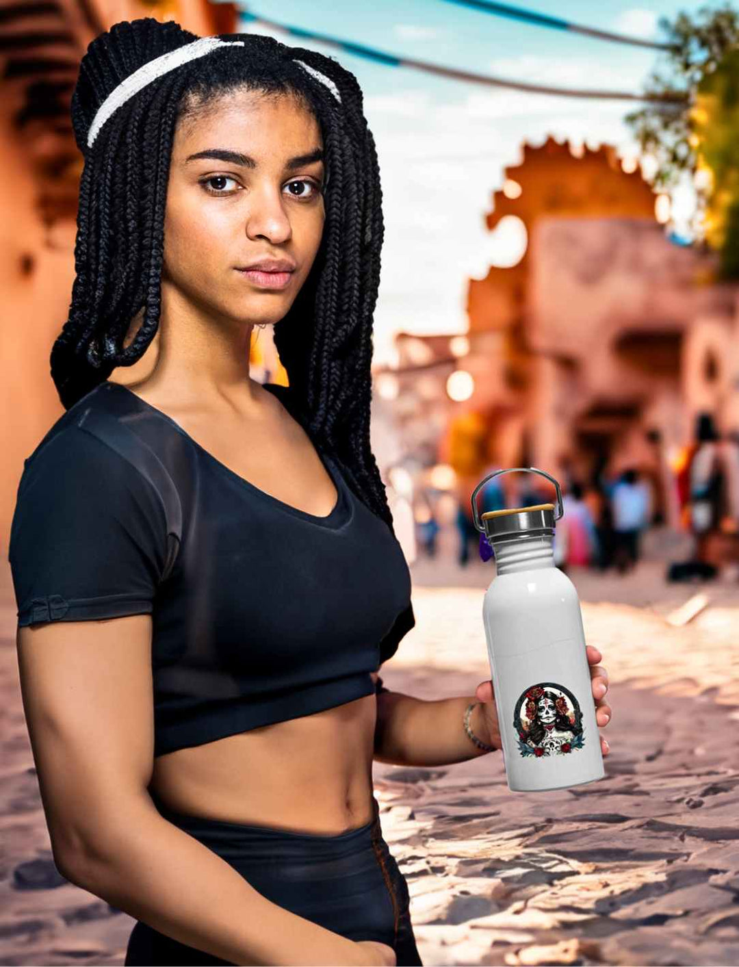 Junge Frau hält die La Catrina Edelstahl Trinkflasche in Emaille-Optik, stehend auf einer charakteristischen mexikanischen Straße während des Dia de los Muertos – Runental.de