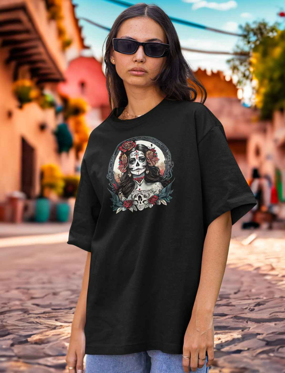 Junge Frau trägt La Catrina Organic Oversized T-Shirt in elegantem Schwarz, posiert vor einer typisch mexikanischen Straße während des Día de los Muertos – Runental.de