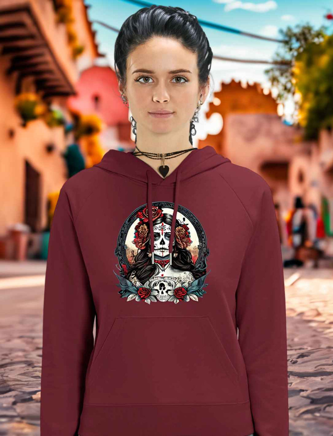 Junge Frau trägt La Catrina Organic Damen Hoodie in Burgund, stehend auf einer charakteristischen mexikanischen Straße am Día de los Muertos – Runental.de.