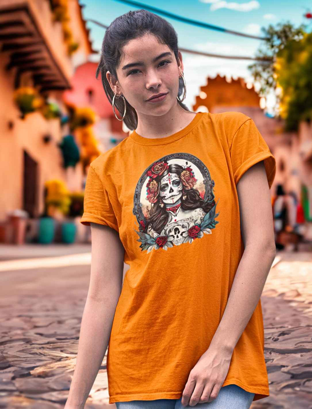 Junge Frau im Orange Unisex La Catrina Shirt, stehend auf einer pittoresken mexikanischen Straße am Dia de los Muertos – Runental.de.