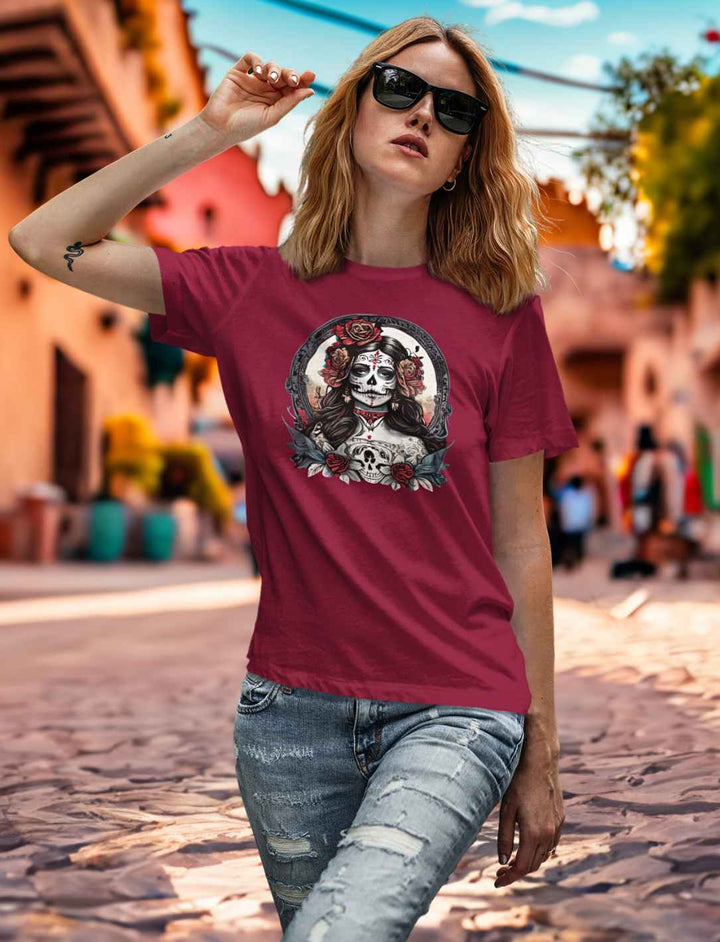 Junge Frau im La Catrina Damen Shirt in reichem Burgund, inmitten einer ruhigen mexikanischen Straße, dekoriert für den Día de los Muertos – Runental.de.
