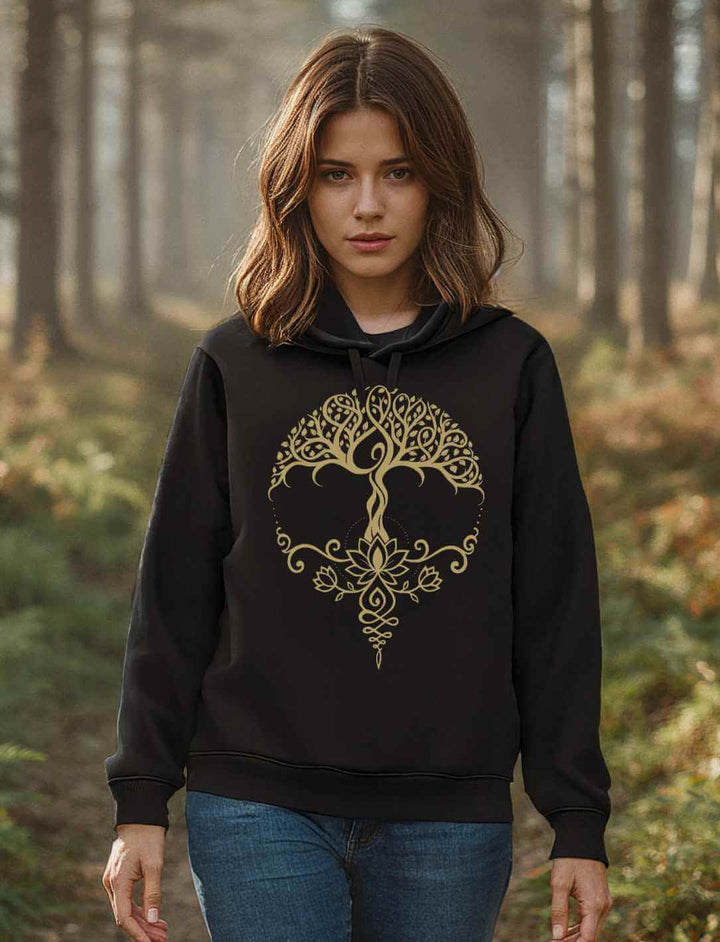 Junge Frau steht im Wald, trägt einen schwarzen Bio-Hoodie mit goldfarbenem Lebensbaum- und Lotus-Design auf der Brust, lange Ärmel, Kapuze auf dem Rücken.