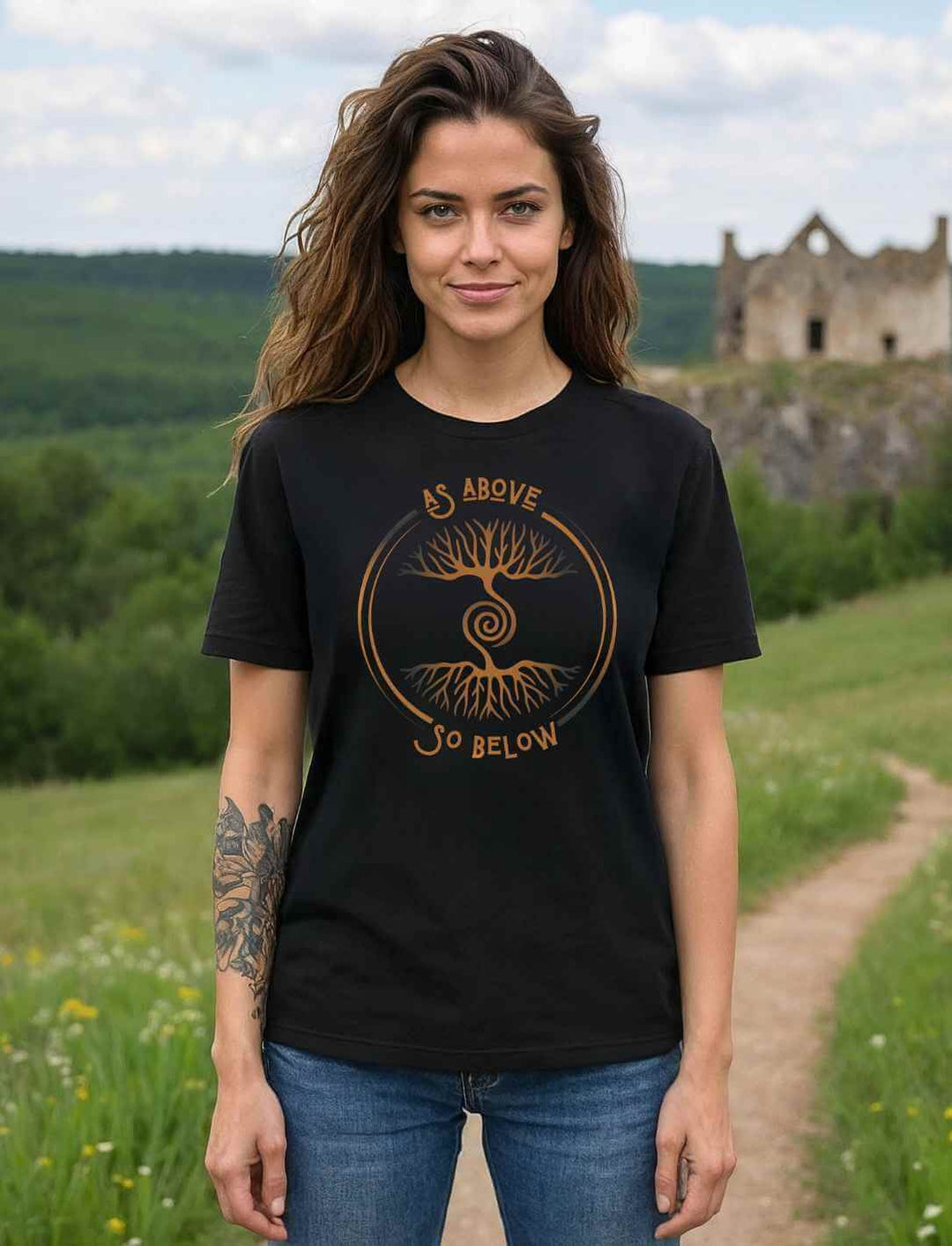 Frau trägt schwarzes Unisex Organic T-Shirt „Lebenswurzel der Verbundenheit“ mit Weltenbaum-Motiv auf Waldweg