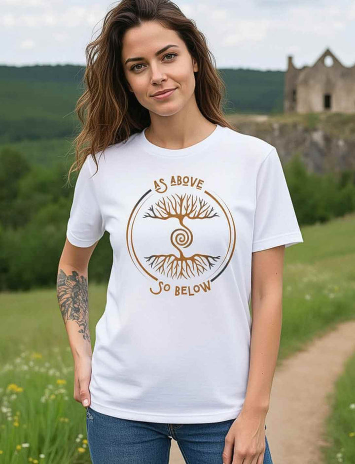 Frau trägt weißes Unisex Organic T-Shirt „Lebenswurzel der Verbundenheit“ mit goldfarbenem Weltenbaum-Motiv vor Naturkulisse