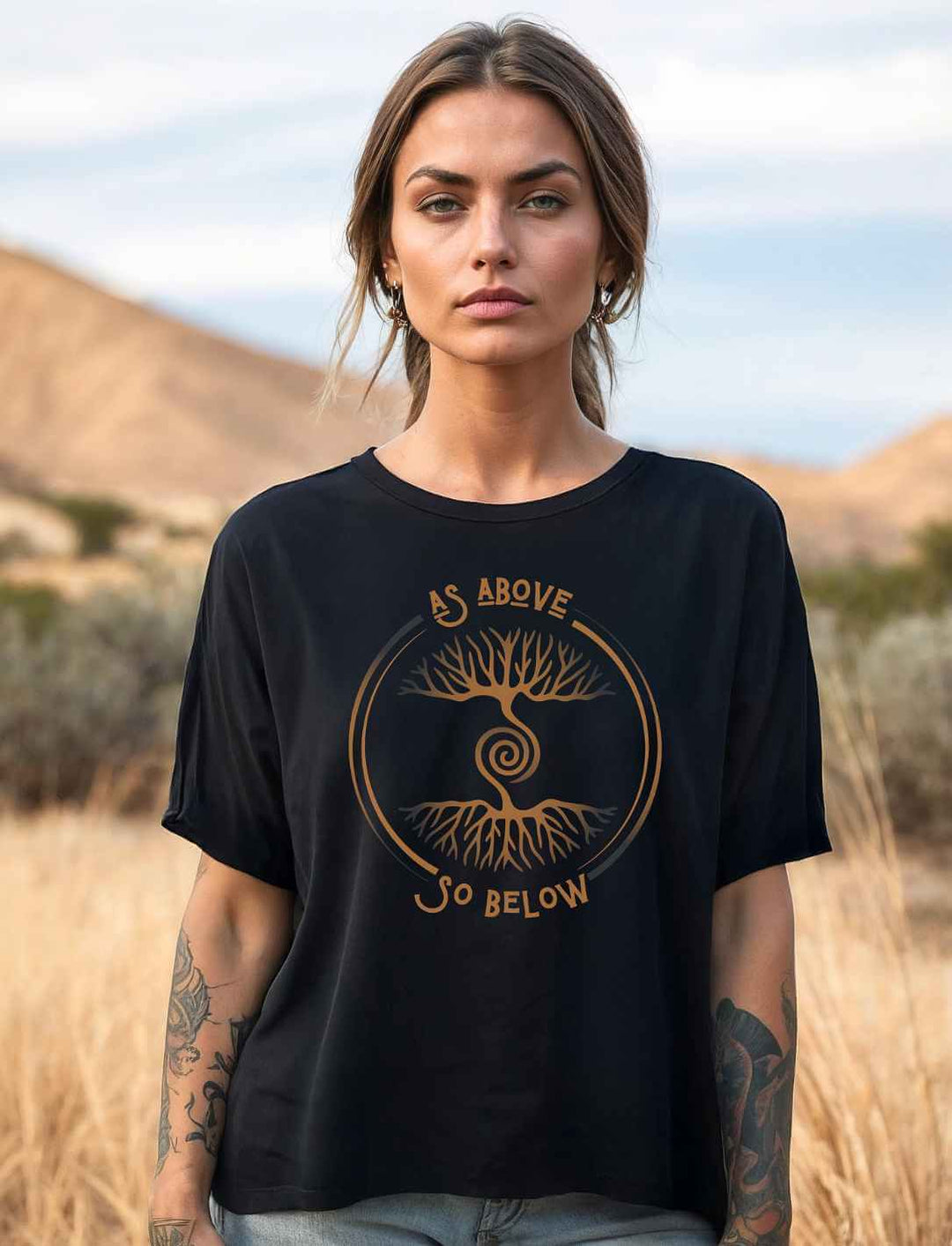 Frau trägt schwarzes Damen Relaxed Shirt „Lebenswurzel der Verbundenheit“ mit kupferfarbenem Weltenbaum-Motiv in der Natur