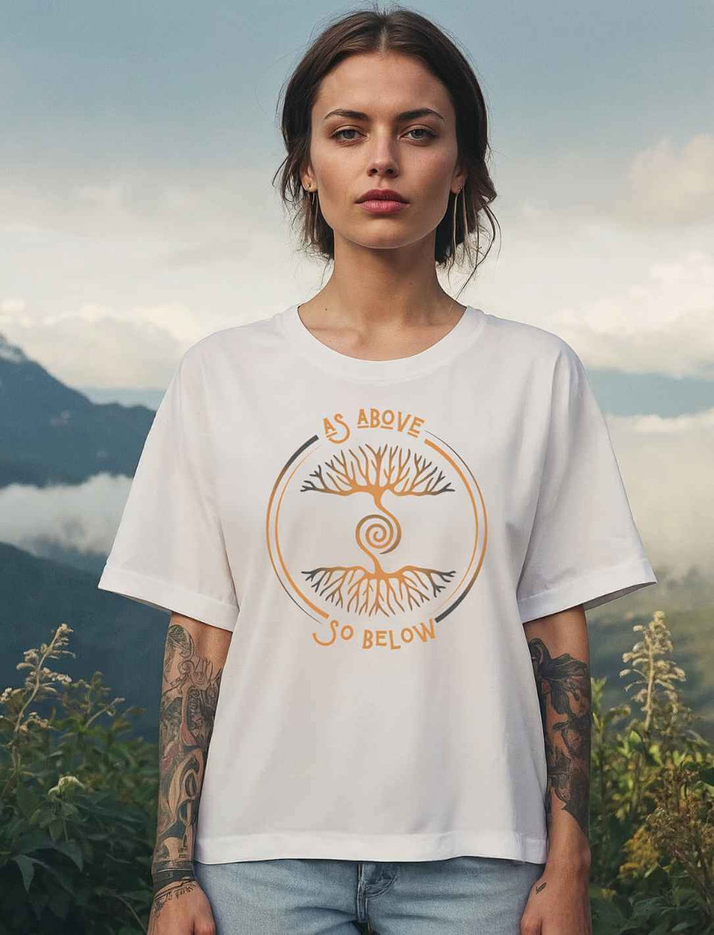 Frau trägt weißes Damen Relaxed Shirt „Lebenswurzel der Verbundenheit“ mit goldfarbenem Aufdruck „As Above, So Below“ vor Bergkulisse