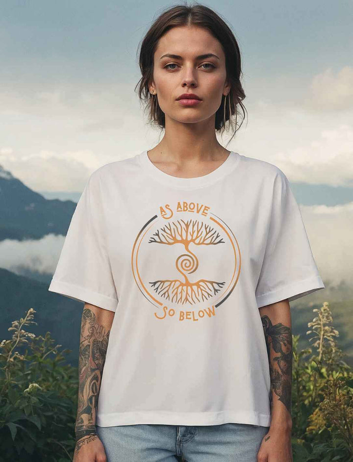 Frau trägt weißes Damen Relaxed Shirt „Lebenswurzel der Verbundenheit“ mit goldfarbenem Aufdruck „As Above, So Below“ vor Bergkulisse