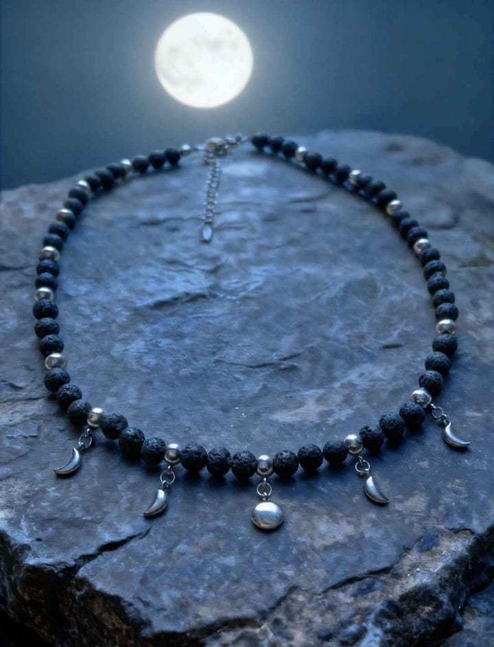 unatic Dreams Mondphasen-Kette aus Lavastein und Edelstahl, präsentiert auf Fels unter hellem Vollmond.