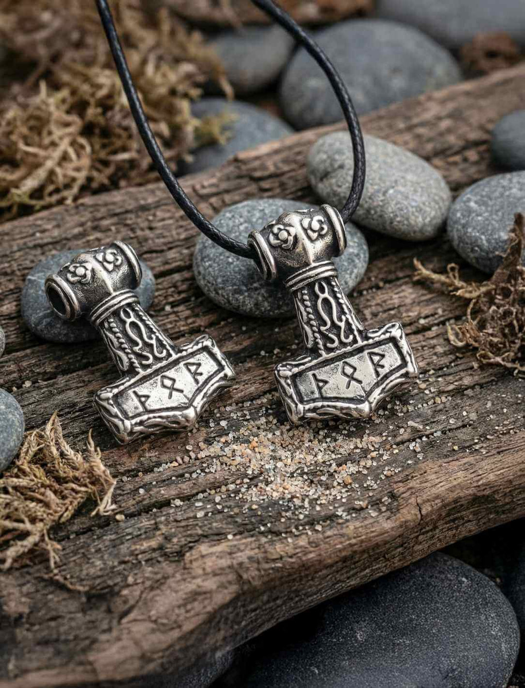 Zwei antik oxidierte Mjölnir Silberanhänger mit Runengravur auf dunklen Flusssteinen