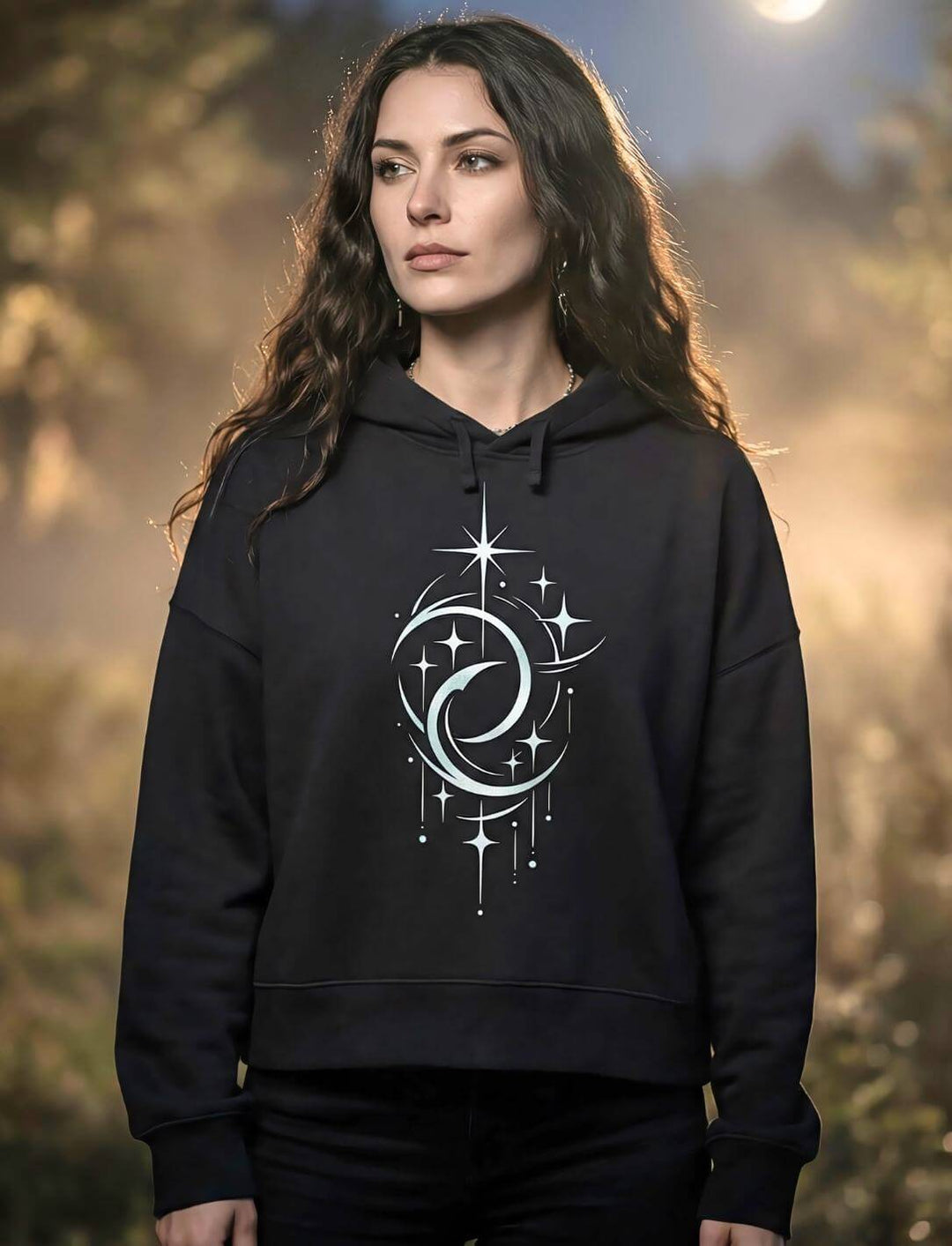 Frau mit dunklen Haaren trägt schwarzen Mondphasen Boxcut Hoodie mit Doppelmond Sternenmotiv vor nebligem Wald bei Vollmond