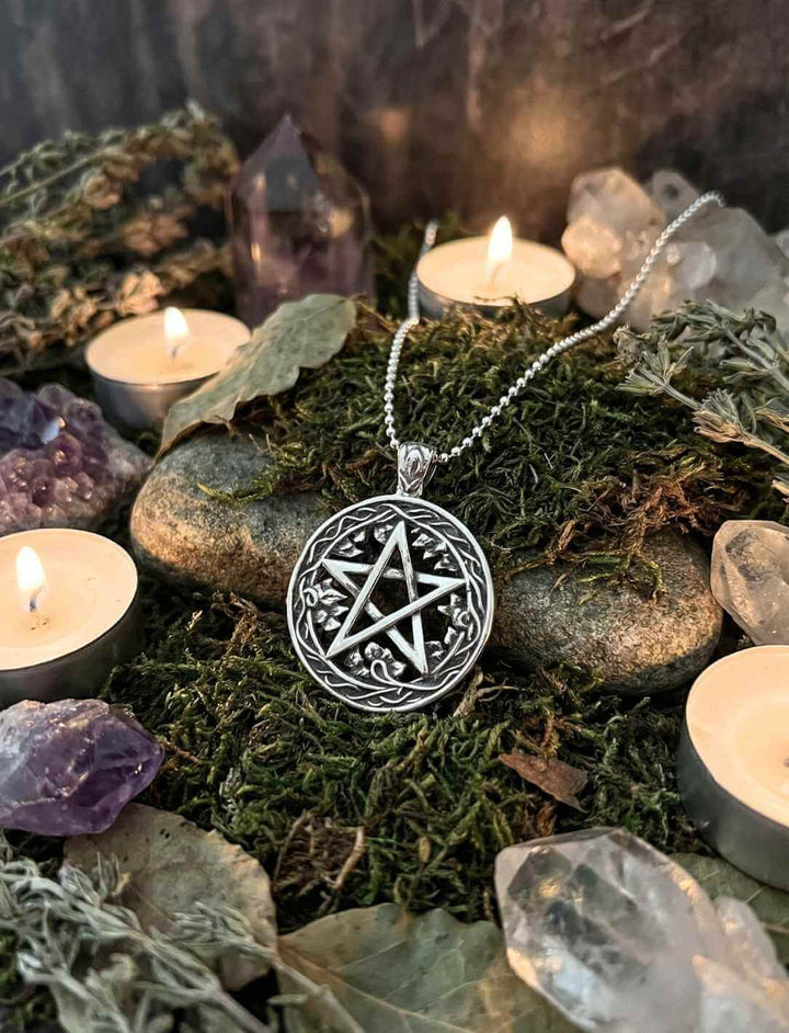 Silberanhänger mit aufrechtem Pentagramm im Kreis, arrangiert mit Kerzen und Natursteinen