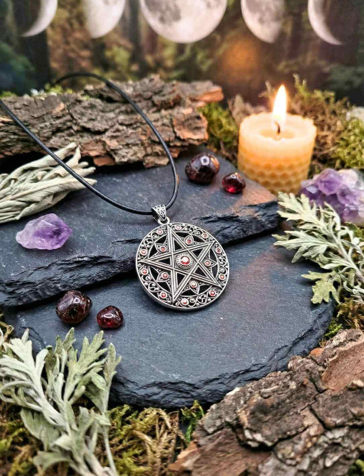 Pentakel Silberanhänger mit roten Zirkonia auf schwarzer Schieferplatte neben Kerze, Kristallen und Kräutern – Wicca Schutzamulett der fünf Elemente