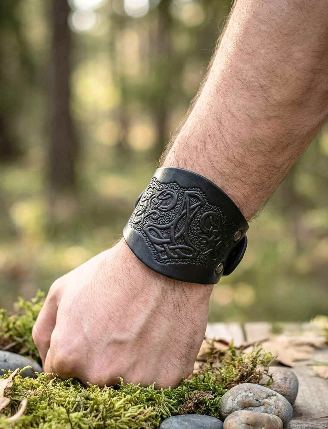 Schwarzes Wikinger Lederarmband, getragen an Handgelenk, mit Mjölnir Symbol im Waldsetting