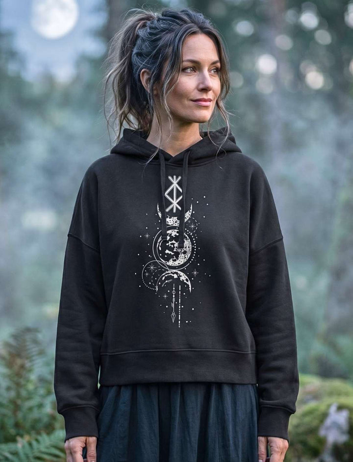 Frau trägt schwarzen Damen Boxcut Hoodie mit nordischer Binderune und Mondphasen-Motiv im nebligen Wald