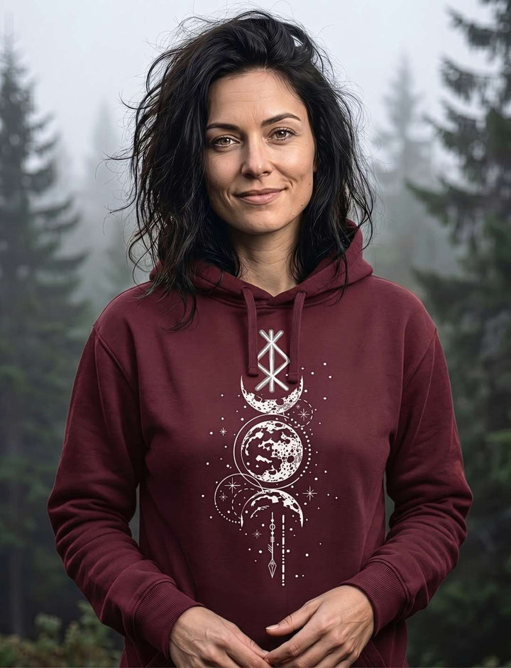 Frau mit dunklem Haar trägt weinroten Runen Hoodie mit Mond-Symbolik vor nebligem Kiefernwald