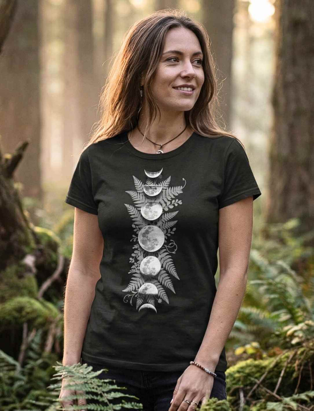 Sacred Moon – Forest Mysteries Damen Organic Shirt in Schwarz mit Mondphasen und Farnmotiv, getragen von Frau im Wald