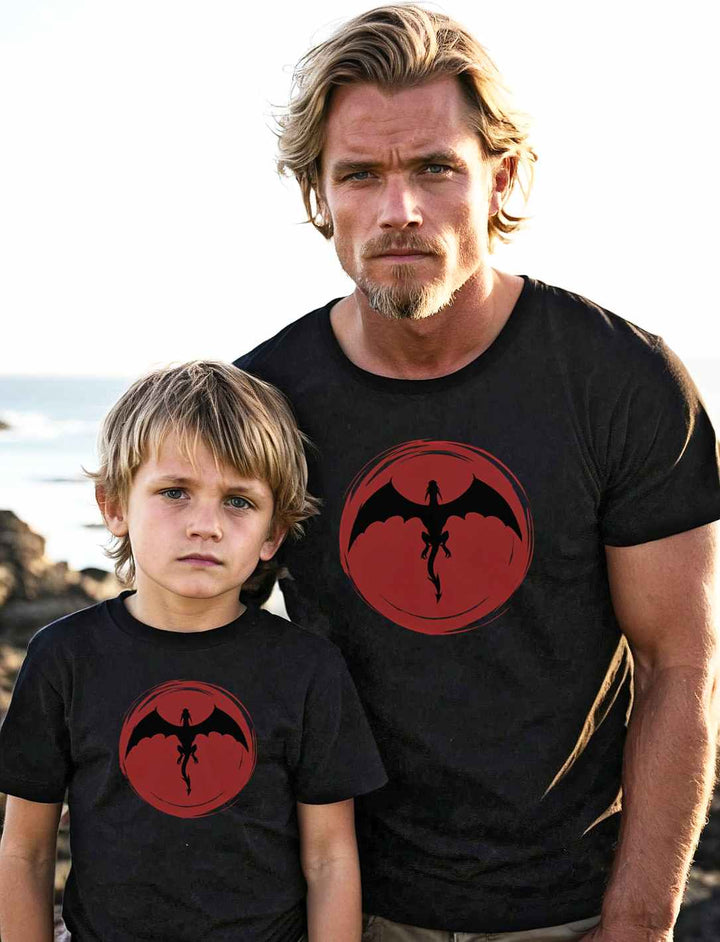 Vater und Sohn stehen nebeneinander am Strand, beide tragen schwarze 'Saga of the Dragon' T-Shirts, und verkörpern die Verbundenheit zwischen den Generationen und den gemeinsamen Abenteuergeist.