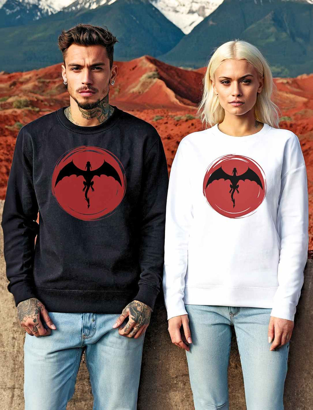 Junger Mann und junge Frau in 'Saga of the Dragon' Sweatshirts in Schwarz und Weiß posieren vor einer dramatischen Landschaft aus Bergen und Wüste, die Energie alter Sagen ausstrahlend.