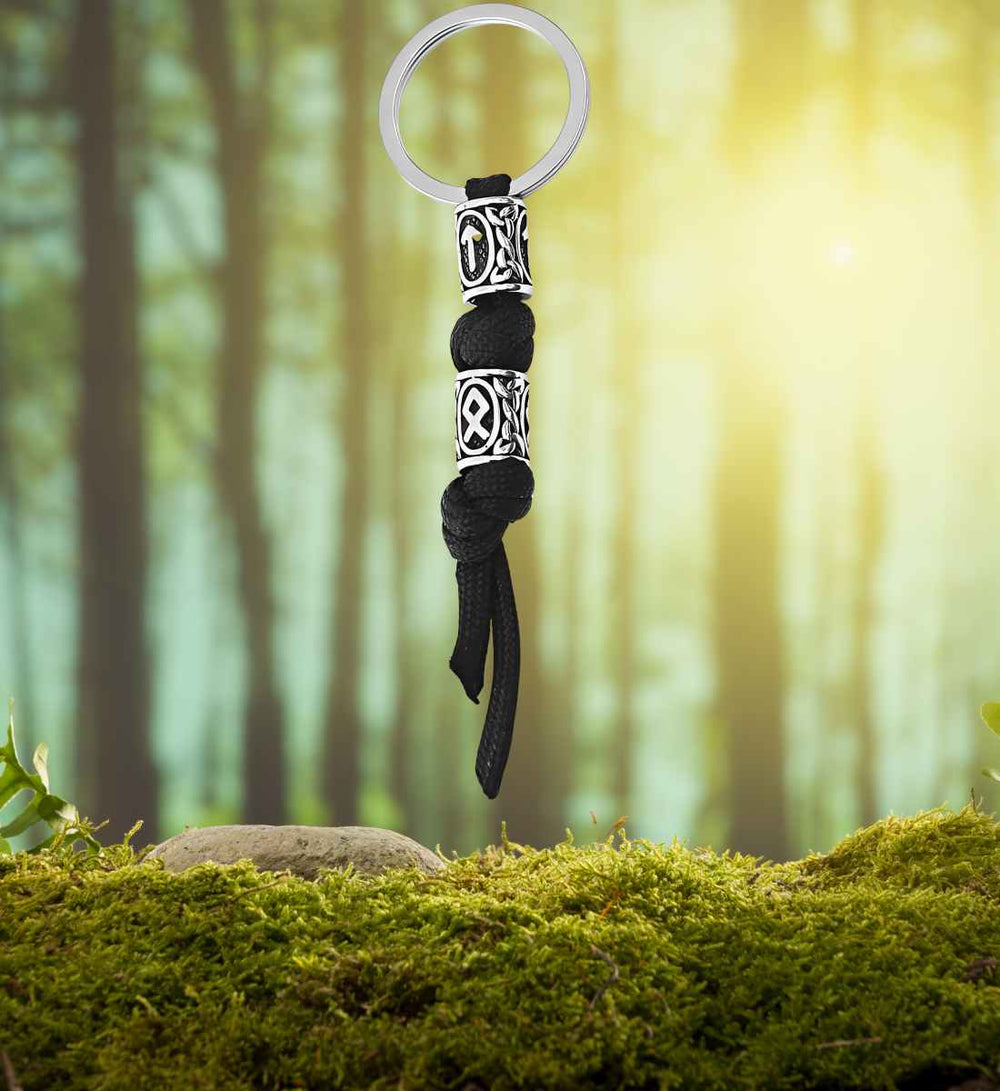 Schlüsselanhänger von Tyr – Paracord-Schlüsselanhänger mit Runenverzierungen aus Edelstahl auf Moos/Wald Hintergrund