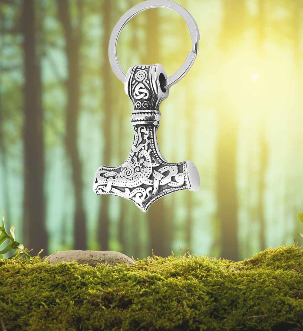 chlüsselring des Mjölnirs – Edelstahl-Schlüsselanhänger in Form von Thor's Hammer mit nordischen Verzierungen auf Wald/Moos Hintergrund.