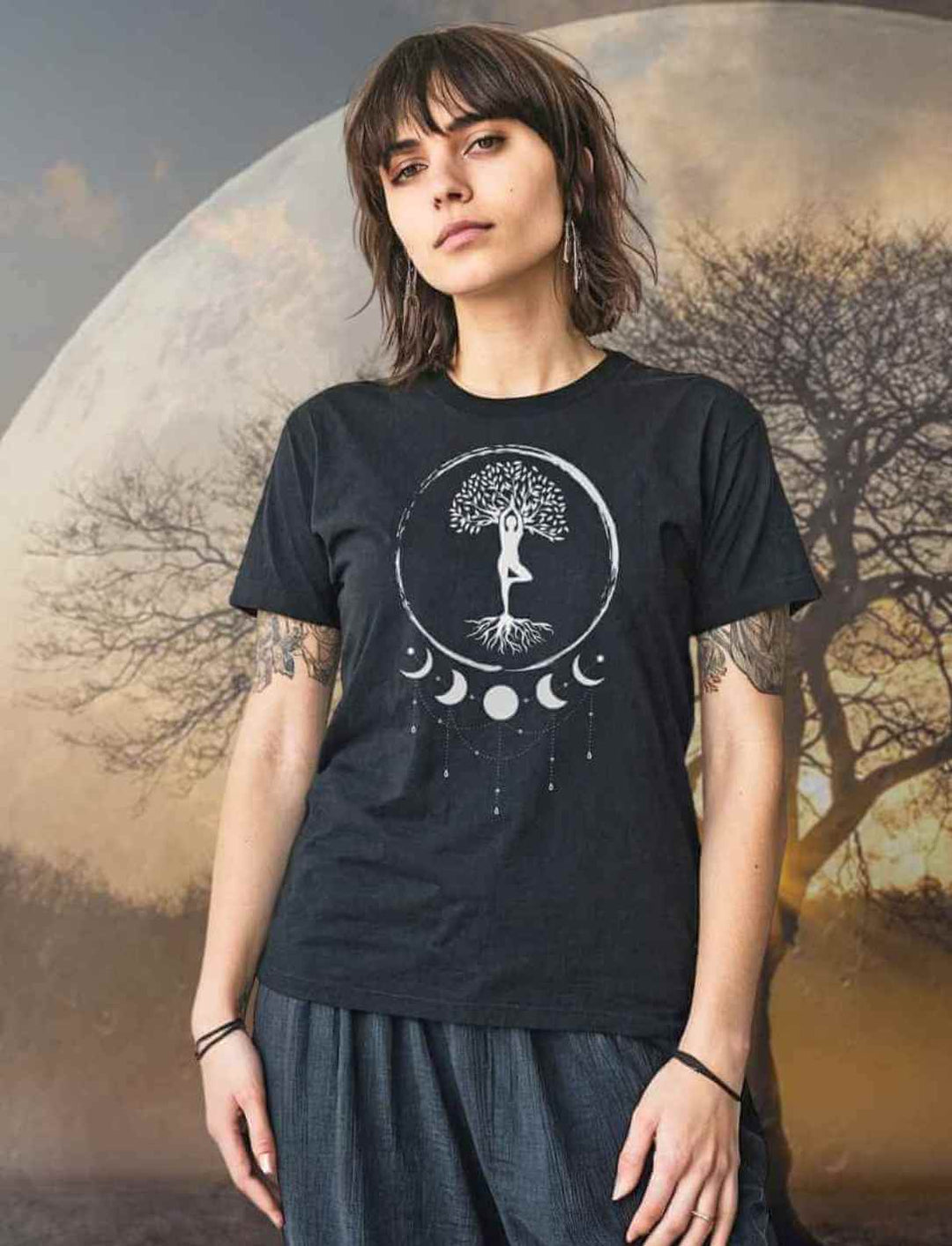 Junge Frau trägt das schwarze Damen T-Shirt Seelenbaum-der-Mondträumer. Im Hintergrund ist ein mystischer Mond und ein Lebensbaum zu sehen.