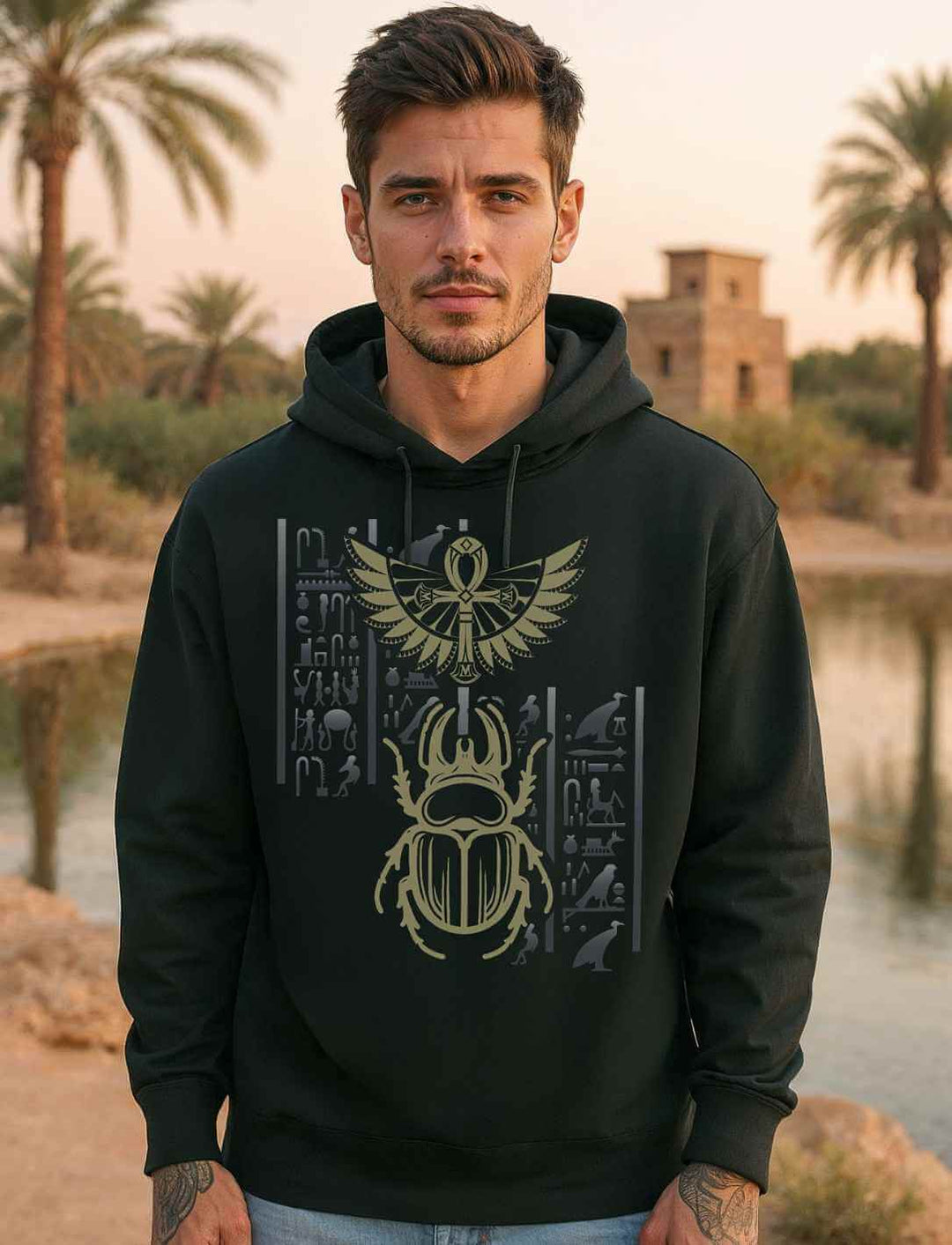 Männliches Model trägt schwarzen Bio-Hoodie mit goldenem Skarabäus-Motiv vor ägyptischer Landschaft