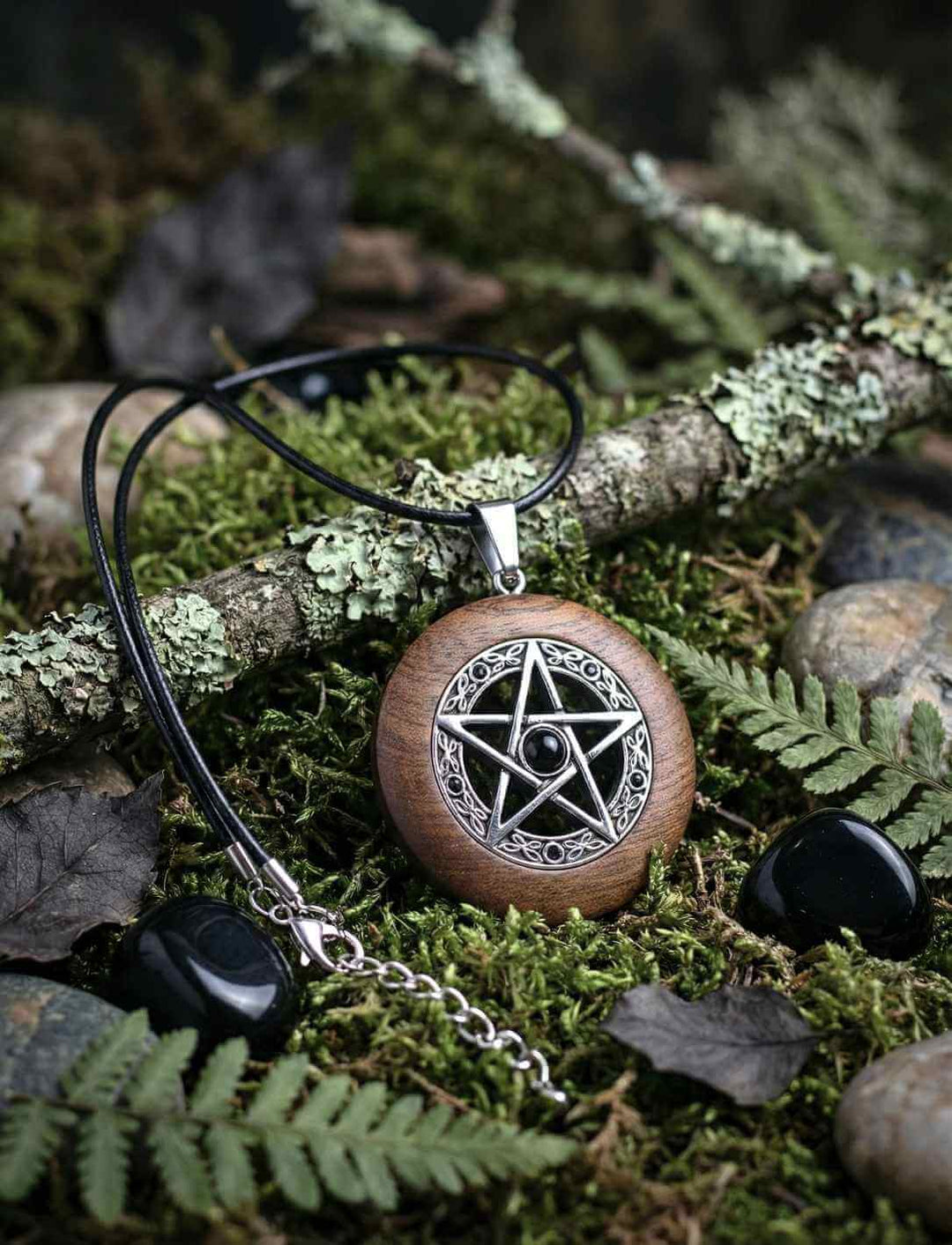 Holzanhänger mit Pentagramm aus Edelstahl und Onyx, liegend auf moosigem Waldboden im Natursetting, mit dünner Lederkette.