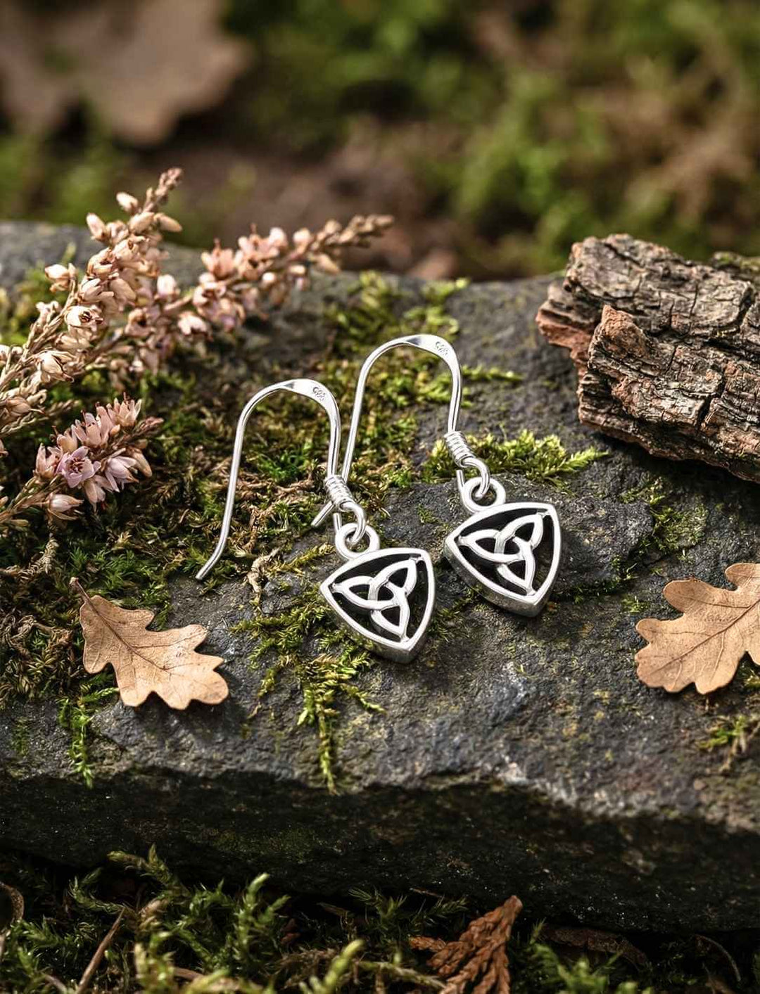 The Quiet Knot Triquetra Ohrhänger aus Silber auf Moos und Stein in Naturkulisse