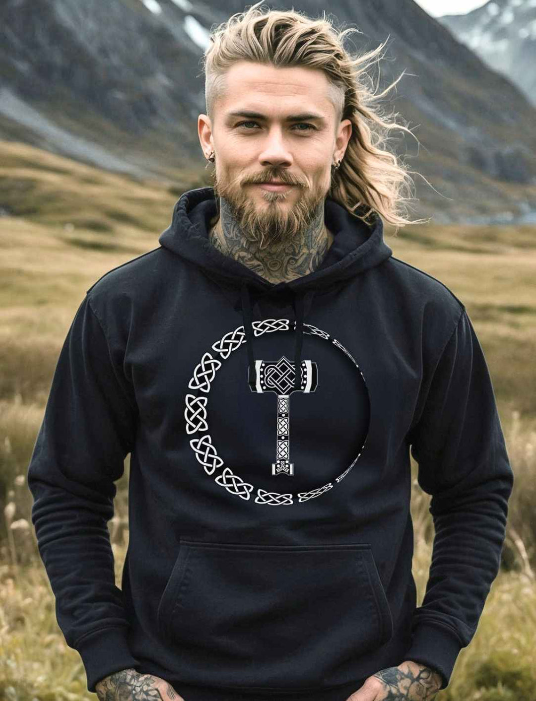 Ein junger Mann, im Wikingerstil, trägt den „Thors Legacy“ Unisex Organic Hoodie in Schwarz und steht inmitten einer atemberaubenden nordischen Landschaft, die die Essenz der nordischen Mythologie einfängt.