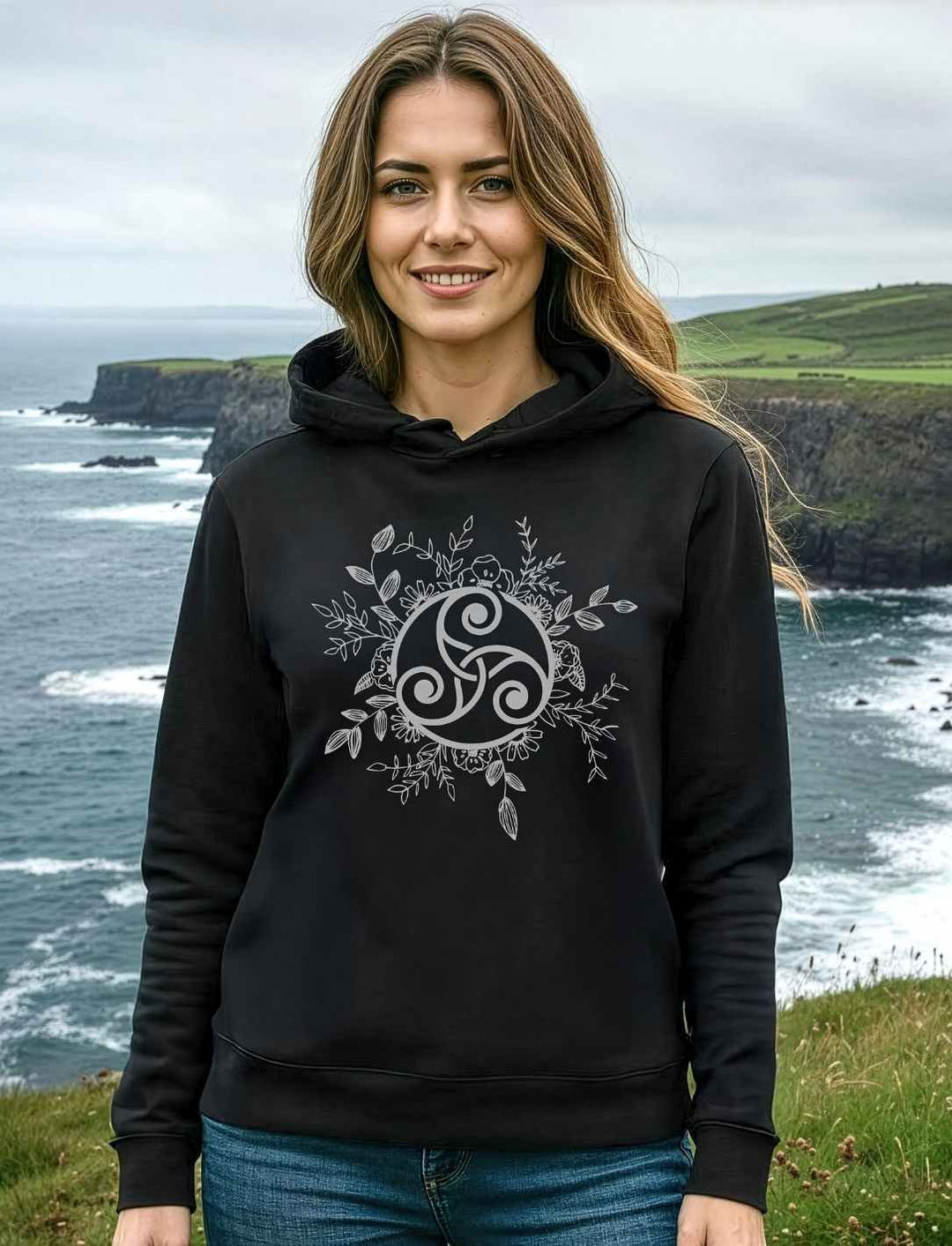 Damen Organic Hoodie Triskele der ewigen Wandlung in Schwarz – getragen von junger Frau am Küstenpfad, keltisches Symbol für Ruhe und Wandel“