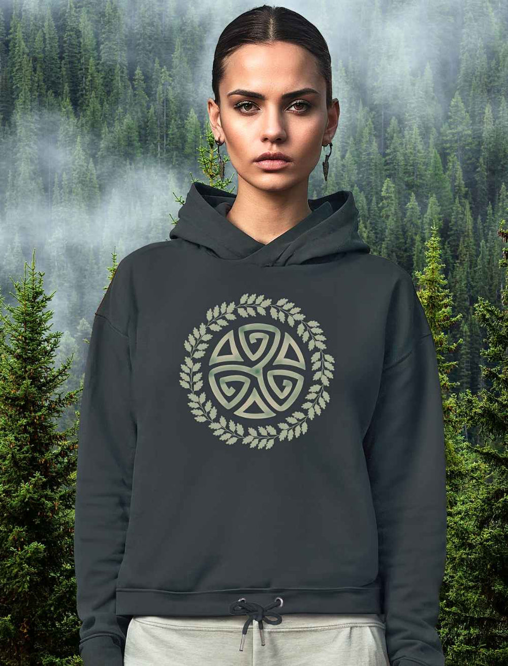 Junge Frau trägt das Triskele des Waldes cropped Hoodie in india ink grey. Im Hintergrund ein mystischer Wald.