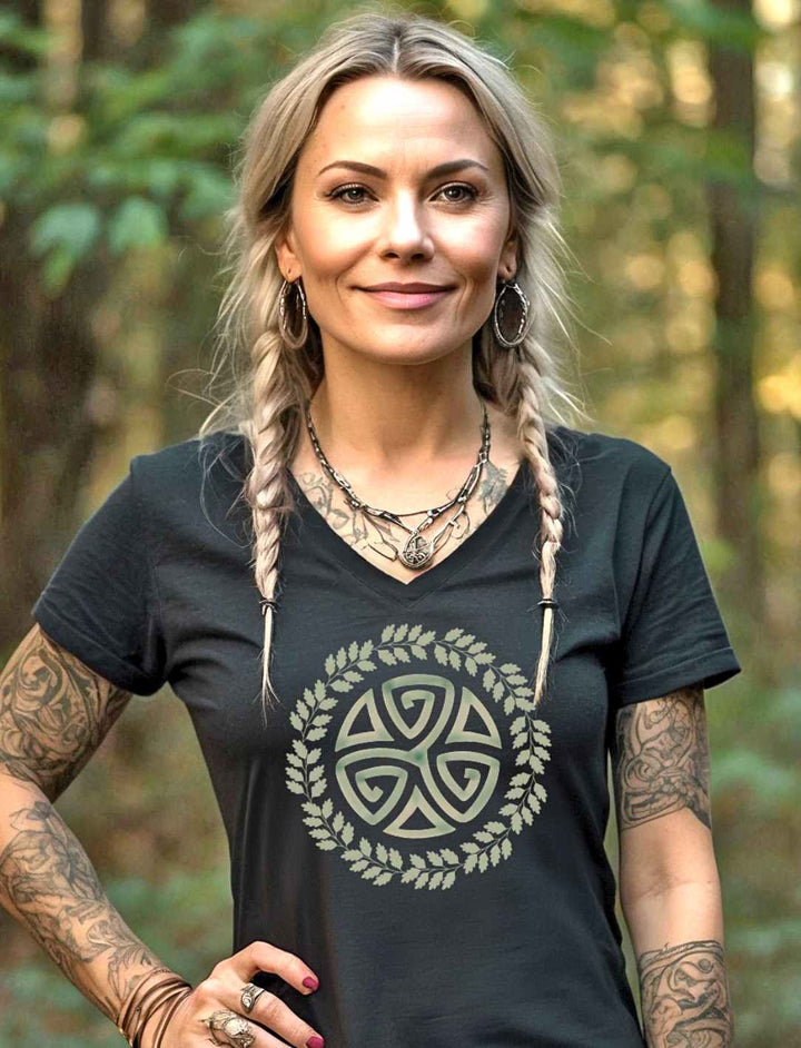 Eine blonde Frau trägt das Triskele des Waldes Damen V-Neck Shirt in Schwarz vor einem Wald Hintergrund – Ein Symbol der Natur und Magie.