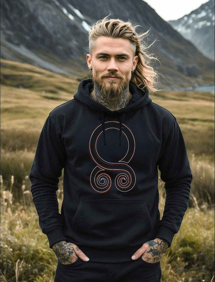 Junger bärtiger Mann im Wikinger Style trägt das Trollbann des Nordes Hoodie. Im Hintergrund eine nordische Landschaft.