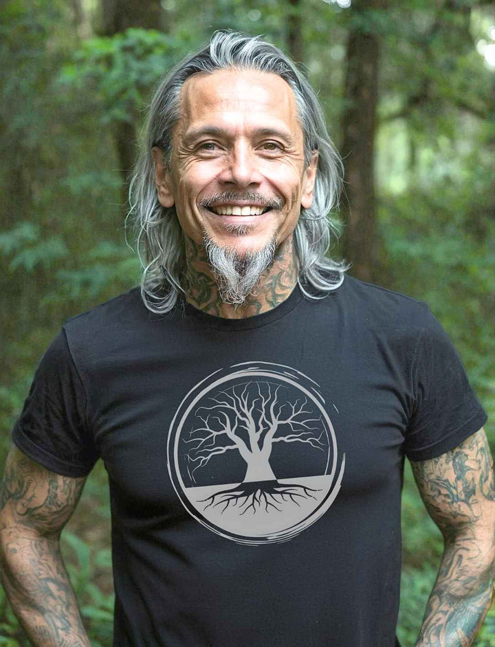 Bärtiger Mann trägt schwarzes Unisex-Shirt im Wald – harmonische Verbindung von Stil und Natur in einem kraftvollen Look.