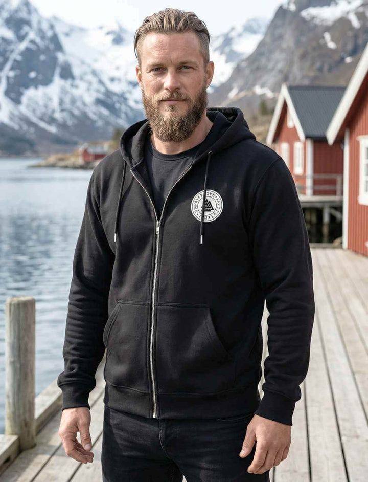 Valknut Zip Hoodie in Schwarz, getragen von Model am Fjord, nordisches Runensiegel auf der Brust, Kapuzenpullover mit Reißverschluss inspiriert von Odin.
